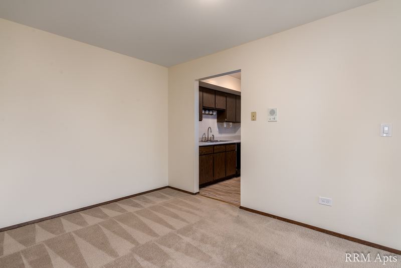 Carpeted living room with cream walls and a doorway to the kitchen, John Mogg apartment 32927 304