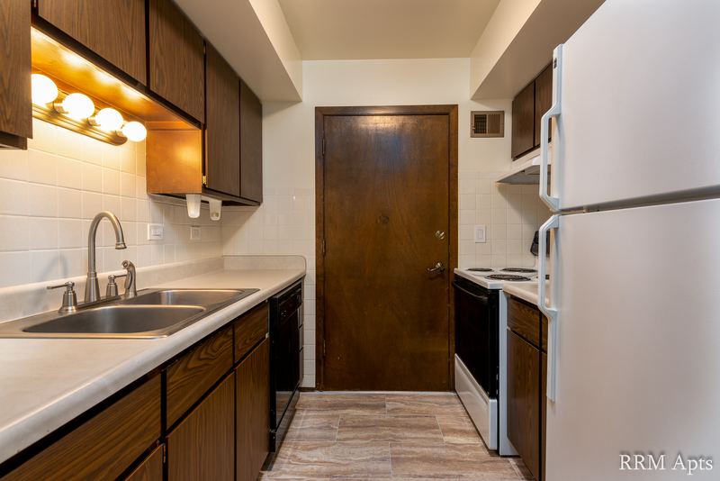 Kitchen with dark wood cabinets, double sink, white refrigerator, white stove and a wood door, John Mogg apartment 32927 304