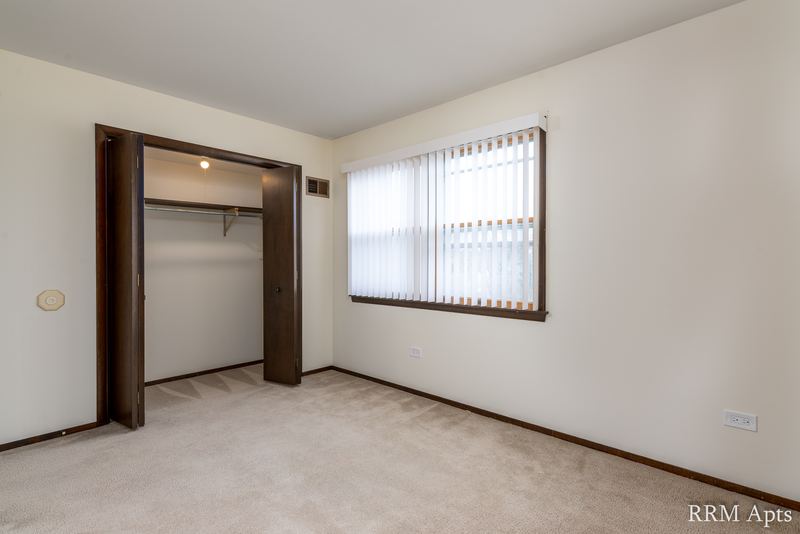 Carpeted bedroom with an open closet with dark wood doors and a window with blinds, John Mogg apartment 32927 304