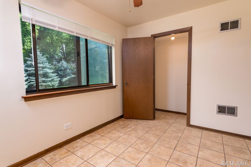 Dining area with tile floor, a wood-trimmed window looking at evergreens and a wood door, John Mogg apartment 32985 102