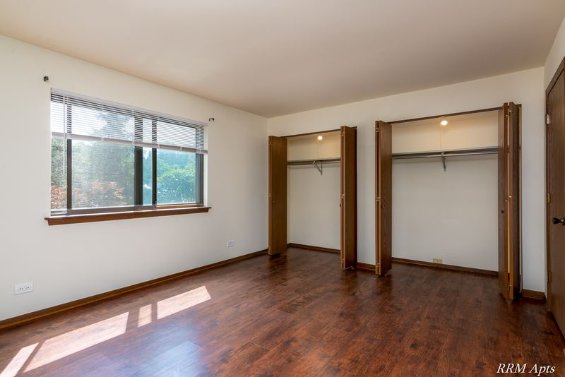 Bedroom with wood floor, two open closets with wood doors and a wood-trimmed window, John Mogg apartment 32985 102