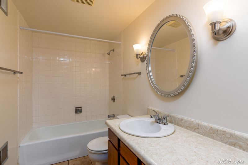 Bathroom with white tile tub surround, toilet, dark wood vanity and oval mirror, John Mogg apartment 32985 102