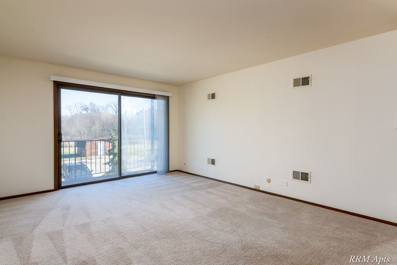 Carpeted living room with cream walls and a sliding glass door to a balcony, John Mogg apartment 32985 201
