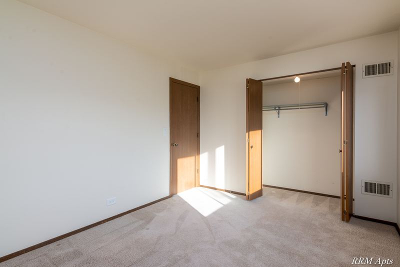Carpeted bedroom with an open closet with wood door and a second wood door, John Mogg apartment 32985 201