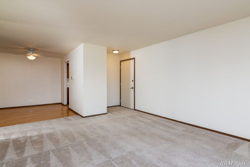 Carpeted living room with cream walls, a white entry door and a hallway beyond, John Mogg apartment 32985 201