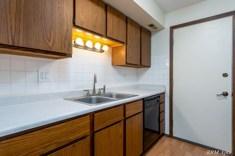 Kitchen with oak cabinets, double sink, black dishwasher, tile backsplash and a white door, John Mogg apartment 32985 201