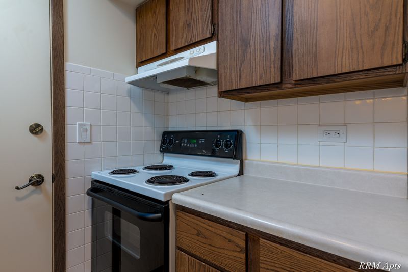 Kitchen with oak cabinets, black electric stove, white tile backsplash and range hood, John Mogg apartment 32985 201
