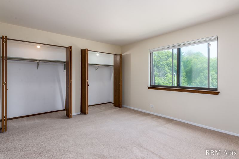 Carpeted bedroom with two open closets and a wood-trimmed window with trees outside, John Mogg apartment 32985 301