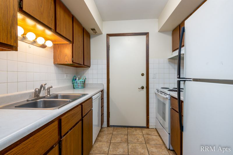 Kitchen with oak cabinets, double sink, white dishwasher, white refrigerator and a white door, John Mogg apartment 32985 301