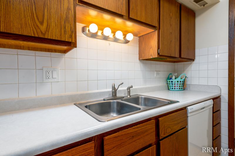 Kitchen with oak cabinets, double sink, white dishwasher, tile backsplash and a light bar, John Mogg apartment 32985 301