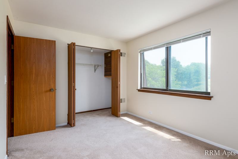 Carpeted bedroom with a wood door, open closet and a wood-trimmed window, John Mogg apartment 32985 301