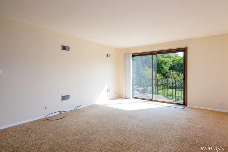 Carpeted living room with sliding glass door to a balcony with iron railing, John Mogg apartment 32985 302