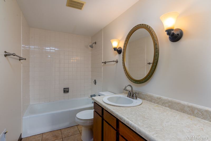 Bathroom with white tile tub surround, wood vanity, oval mirror and sconce lights, John Mogg apartment 32985 302