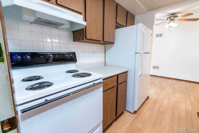 Kitchen with white electric stove and refrigerator, wood cabinets and white tile backsplash, John Mogg apartment 32985 304 N