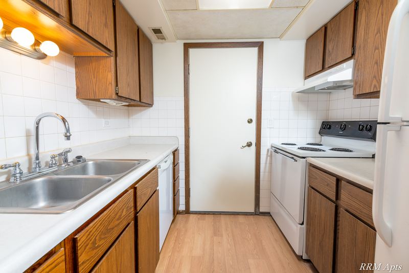 Galley kitchen with wood cabinets, stainless sink, white dishwasher and stove, John Mogg apartment 32985 304 N