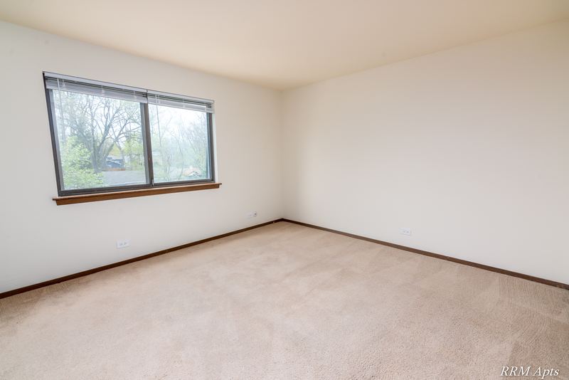 Bedroom with beige carpet and a window looking out on trees, John Mogg apartment 32985 304 N