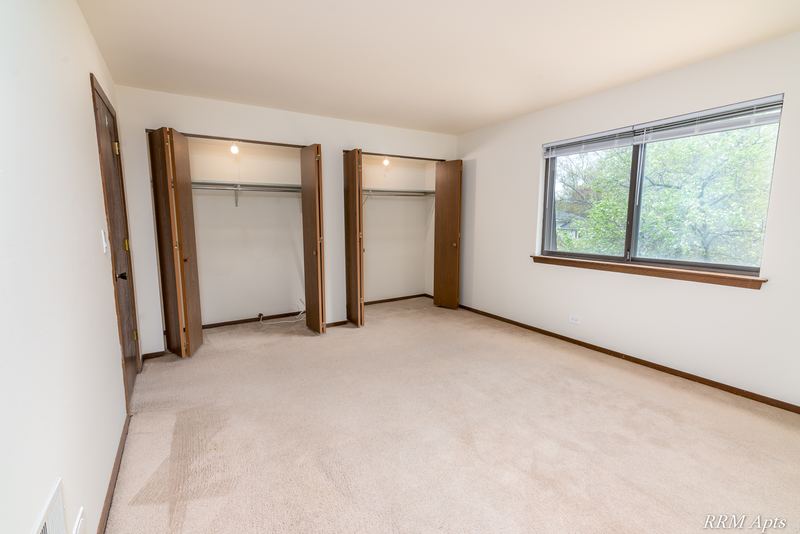 Bedroom with beige carpet, open closet with shelf and a window with trees outside, John Mogg apartment 32985 304 N