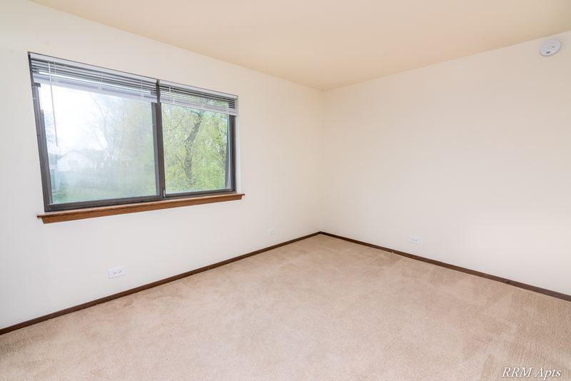 Bedroom with beige carpet and a wide corner window with trees outside, John Mogg apartment 32985 304 N