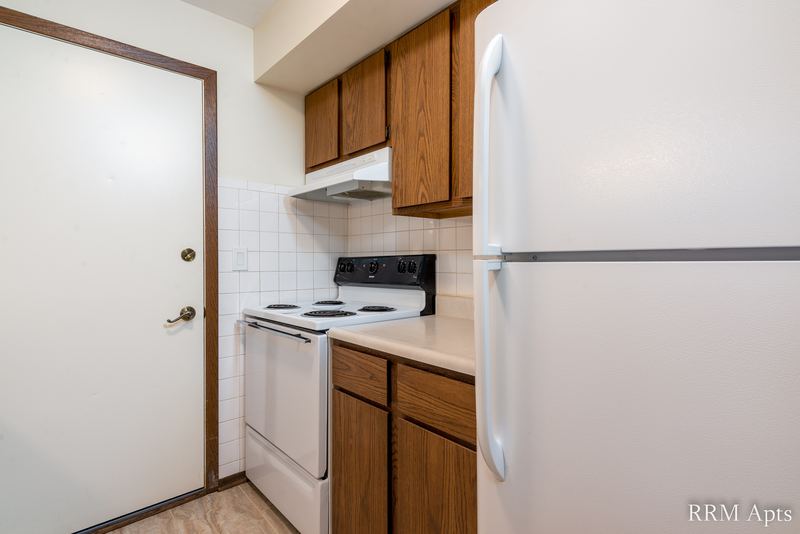 Kitchen with wood cabinets, white electric stove and refrigerator, and the entry door, John Mogg apartment 32985 304
