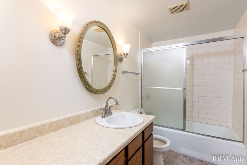 Bathroom with wood vanity, oval mirror, sconce lights and a sliding glass tub door, John Mogg apartment 32985 304