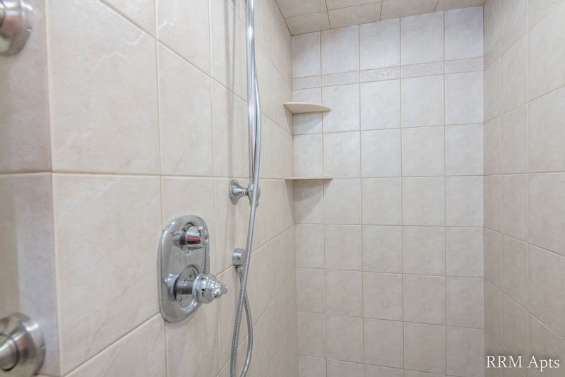 Bathroom with walk-in beige tile shower, corner shelves and a handheld shower head, Maple Avenue apartment 101