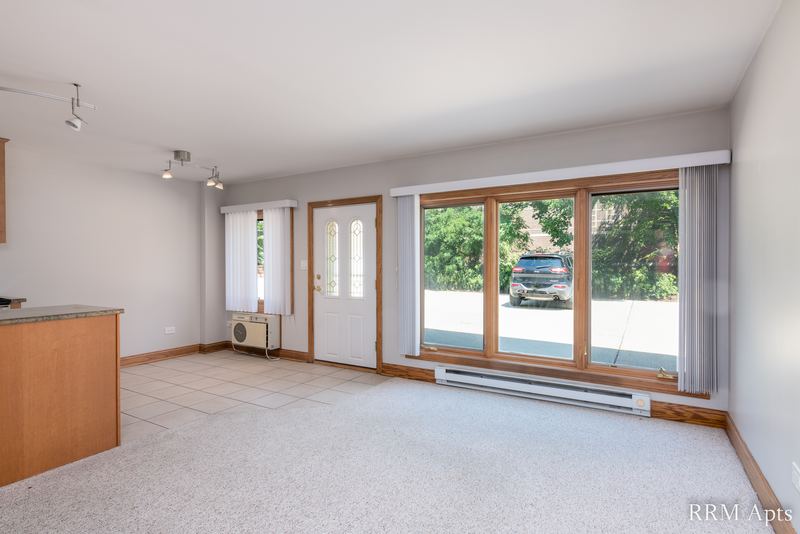 Living room with beige carpet, patio door and windows looking out on parked cars, Maple Avenue apartment 101
