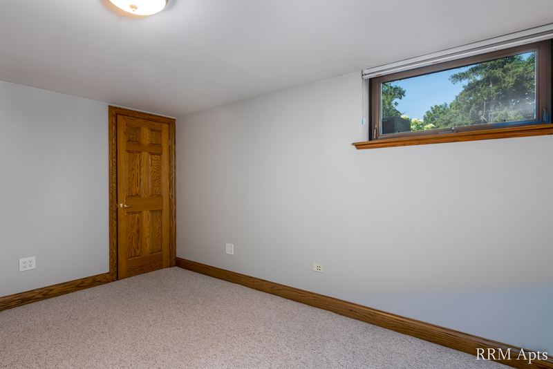 Bedroom with beige carpet, a small high window with trees outside and a wood closet door, Maple Avenue apartment 101