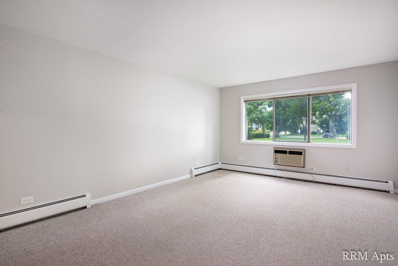 Living room with beige carpet, gray walls, a window with wall air conditioner and baseboard heat, Maple Avenue apartment 1B