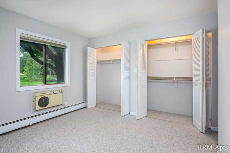 Bedroom with beige carpet, a window with wall air conditioner and two closets with white doors, Maple Avenue apartment 1B