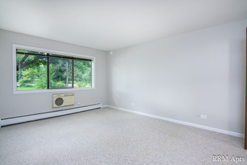 Bedroom with beige carpet and a corner window with wall air conditioner and baseboard heat, Maple Avenue apartment 1B