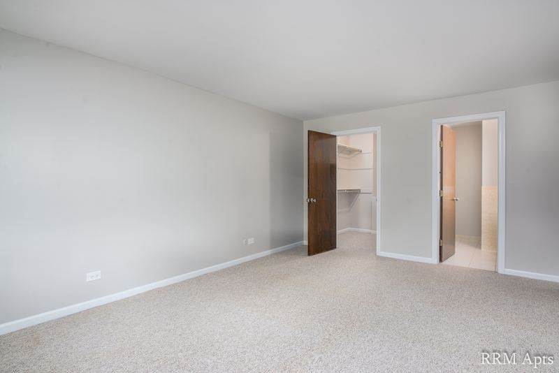 Bedroom with beige carpet, gray walls, a dark wood door and an open closet doorway, Maple Avenue apartment 1B