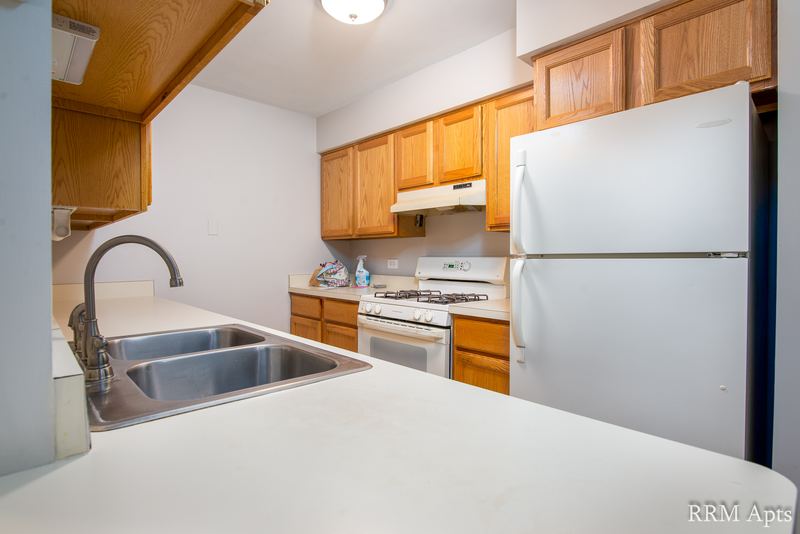 Kitchen with wood cabinets, white refrigerator and stove, stainless double sink and tile floor, Maple Avenue apartment 1B
