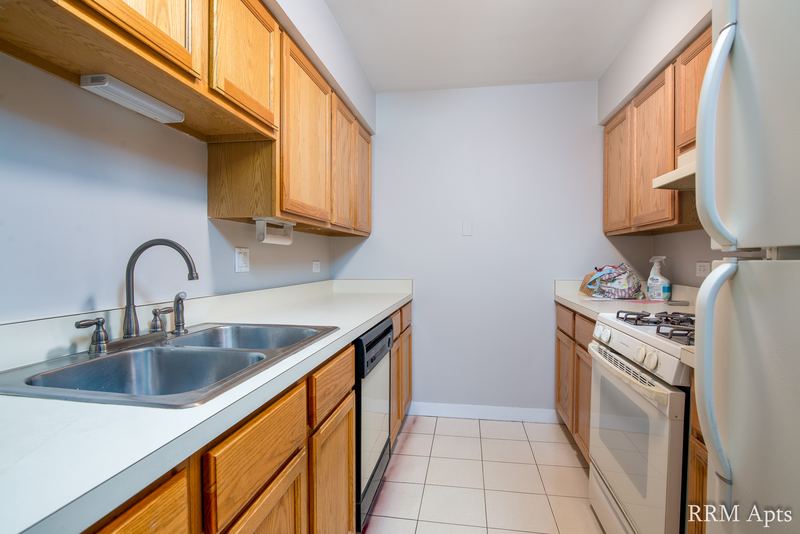 Kitchen with wood cabinets, stainless sink, black dishwasher, white stove and refrigerator, Maple Avenue apartment 1B
