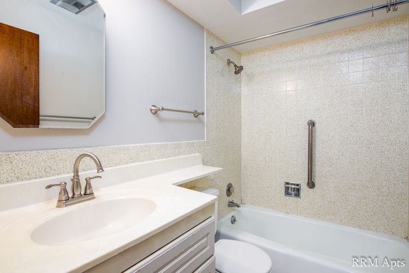 Bathroom with beige tile tub surround, white vanity, grab bars and a wood medicine cabinet, Maple Avenue apartment 1B