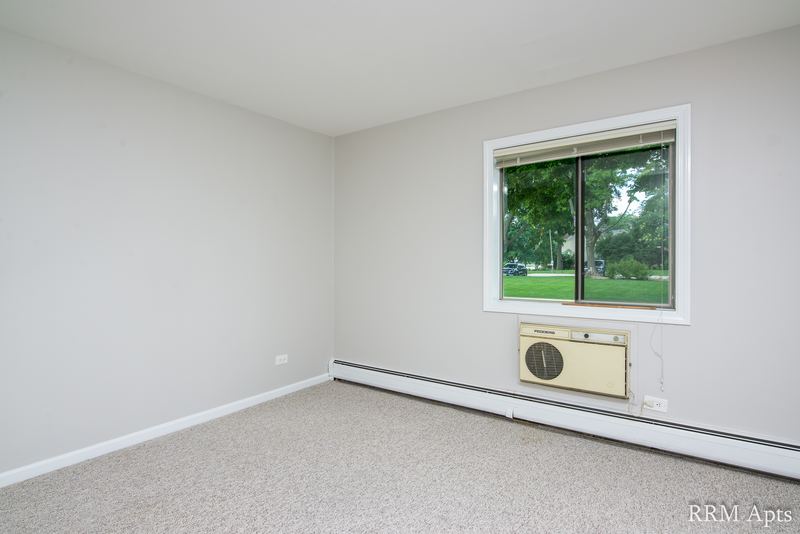 Bedroom with beige carpet, gray walls, a window with wall air conditioner and baseboard heat, Maple Avenue apartment 1B