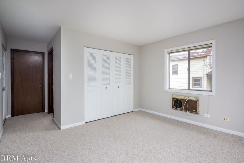 Bedroom with beige carpet, white louvered closet doors, dark wood door and wall air conditioner, Maple Avenue apartment 1E