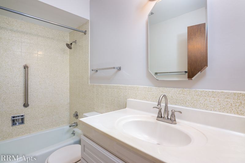Bathroom with beige tile tub surround, white vanity, grab bar and a wood medicine cabinet, Maple Avenue apartment 1E