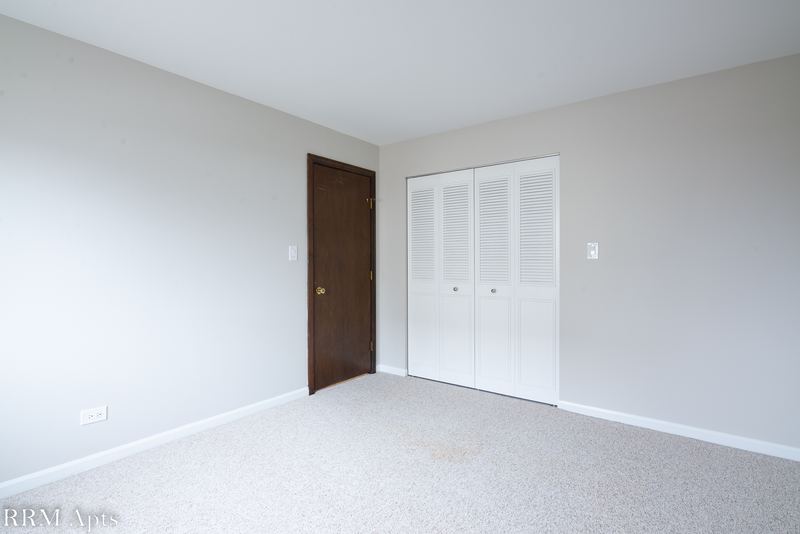 Bedroom with beige carpet, gray walls, dark wood door and white louvered closet doors, Maple Avenue apartment 1E