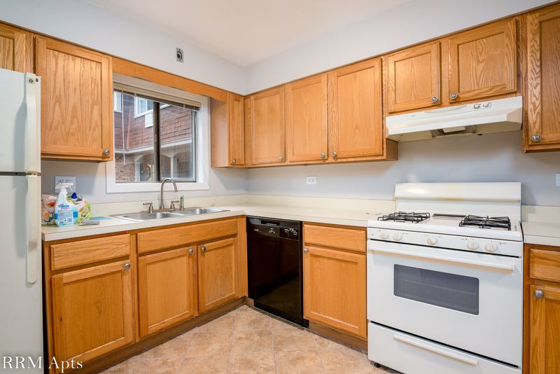 Kitchen with wood cabinets, white refrigerator, black dishwasher, white gas stove and a window, Maple Avenue apartment 1E