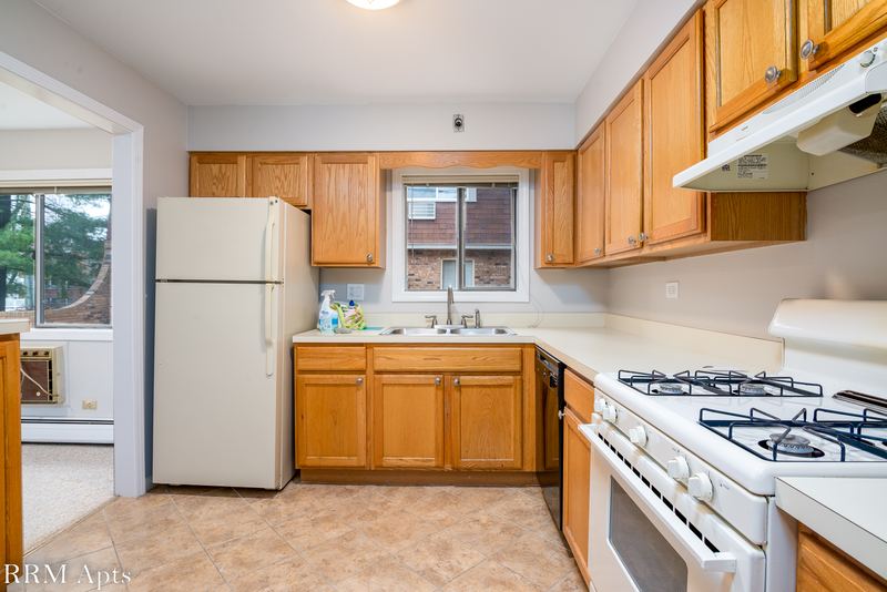 Kitchen with wood cabinets, white refrigerator and stove, a window and doorway to the living room, Maple Avenue apartment 1E