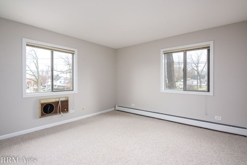 Bedroom with beige carpet, gray walls, two windows with a wall air conditioner and baseboard heat, Maple Avenue apartment 1E