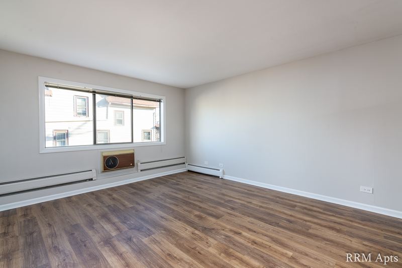 Living room with wood laminate floor, two windows with a wall air conditioner and baseboard heat, Maple Avenue apartment 1F