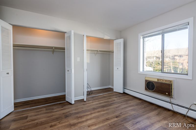 Bedroom with wood laminate floor, two open closets and a window with wall air conditioner, Maple Avenue apartment 1F