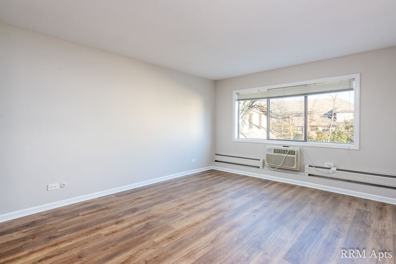 Living room with wood laminate floor and a window with wall air conditioner and baseboard heat, Maple Avenue apartment 1F