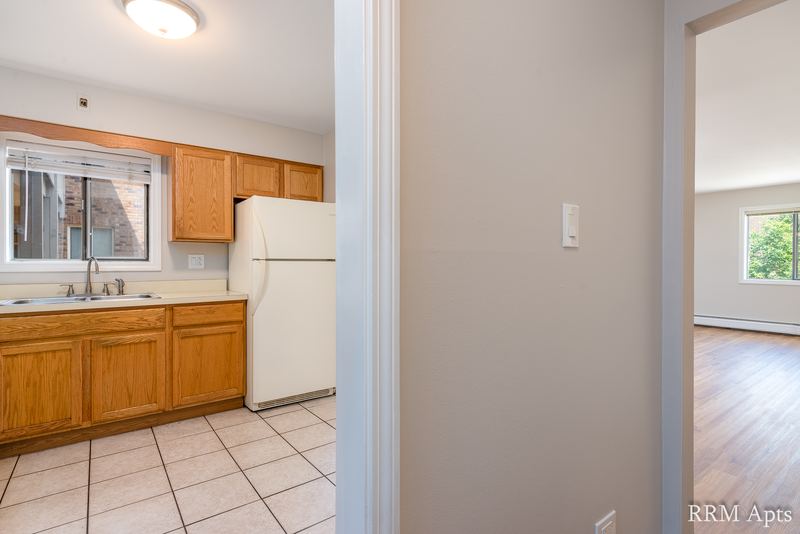 Kitchen with wood cabinets, white refrigerator, window and tile floor, open to the living room, Maple Avenue apartment 1H