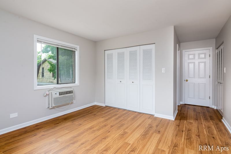 Bedroom with wood laminate floor, wall air conditioner and white louvered closet doors, Maple Avenue apartment 1H