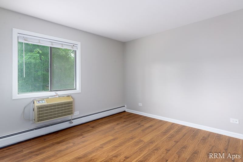 Bedroom with wood laminate floor, a window with trees outside and a wall air conditioner, Maple Avenue apartment 1H