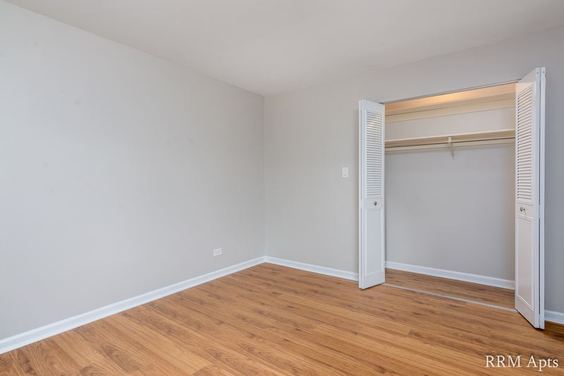 Bedroom with wood laminate floor, gray walls and an open closet with white bifold doors, Maple Avenue apartment 1H