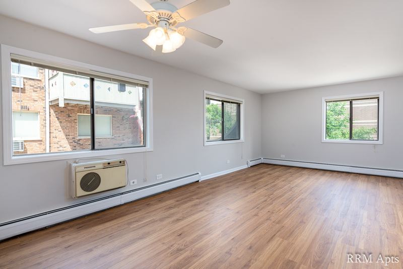 Living room with wood laminate floor, ceiling fan, three windows and a wall air conditioner, Maple Avenue apartment 1H