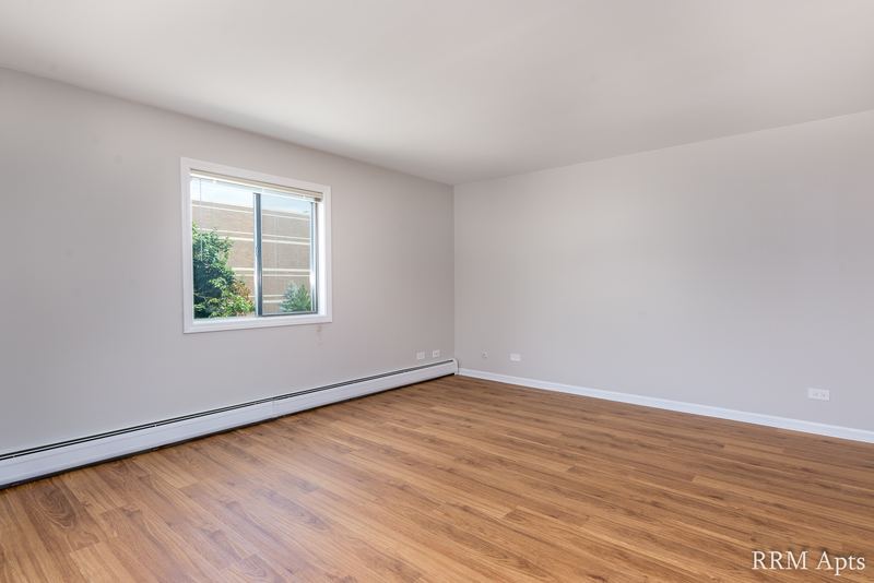 Empty room with wood laminate floor, a single window with trees outside and baseboard heat, Maple Avenue apartment 1H